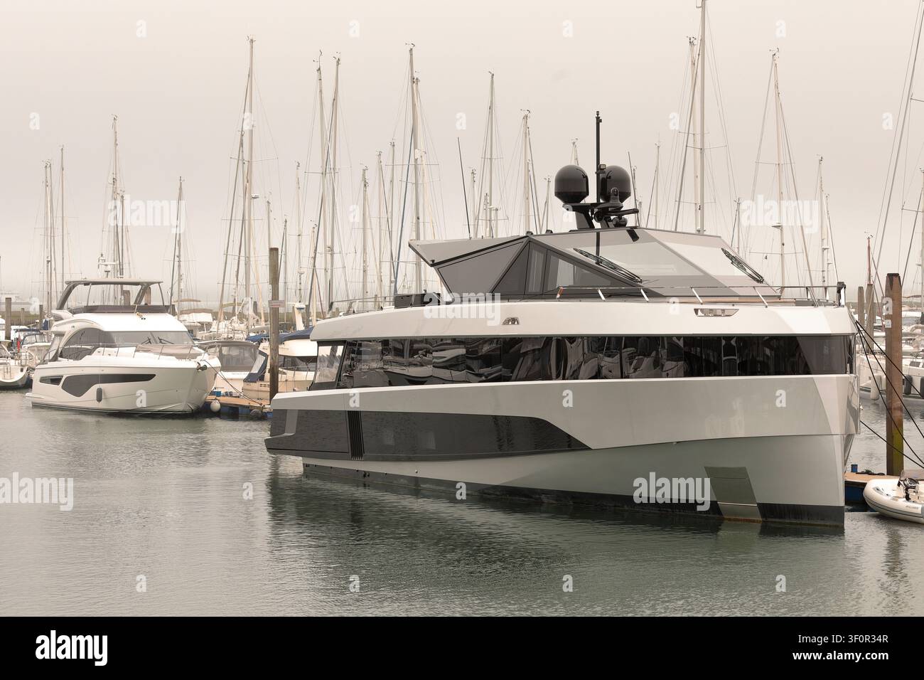 Deux grands yachts à moteur à l'ancre dans une marina avec de nombreux voiliers à l'arrière par une journée grise et nuageuse Banque D'Images