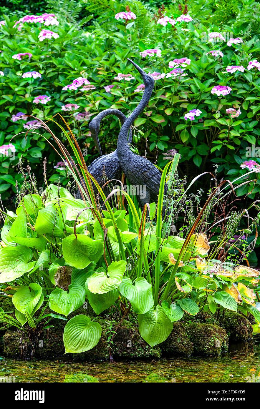 Statues de grues dans l'étang de la carrière à Larmer Tree Gardens dans le Wiltshire, UK, entourées d'un feuillage luxuriant et de fleurs d'été Banque D'Images
