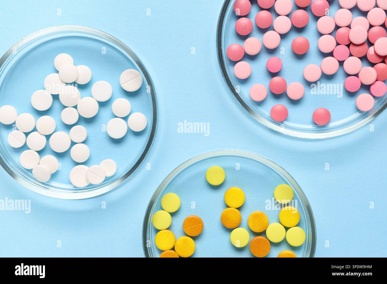 Assortiment de pilules pharmaceutiques blanches, roses et jaunes dans des boîtes de Pétri sur un fond bleu clair, vue de dessus Banque D'Images