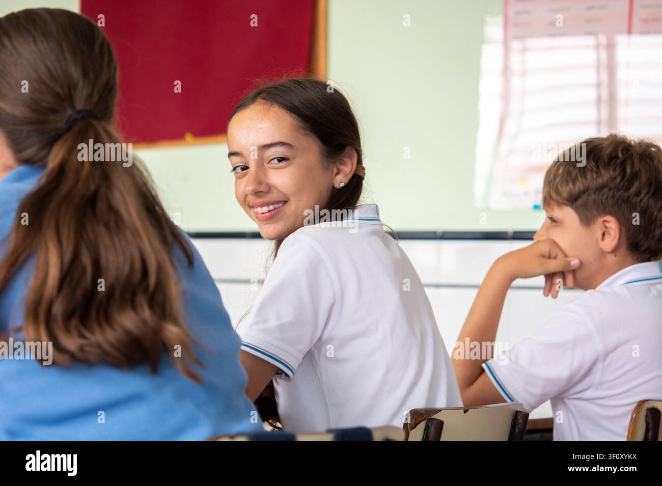 Jeune fille souriante regardant ses camarades de classe pendant une leçon dans une salle de classe lumineuse Banque D'Images