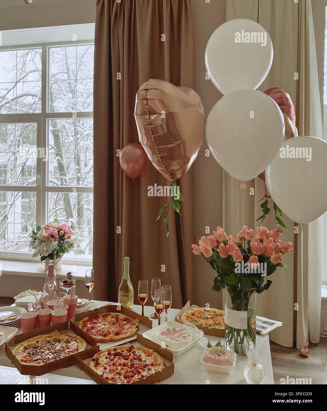 Table d'anniversaire chaleureuse avec pizza, fleurs, ballons, boissons et gâteau près de fenêtres enneigées. - Image de stock capturée avec un smartphone