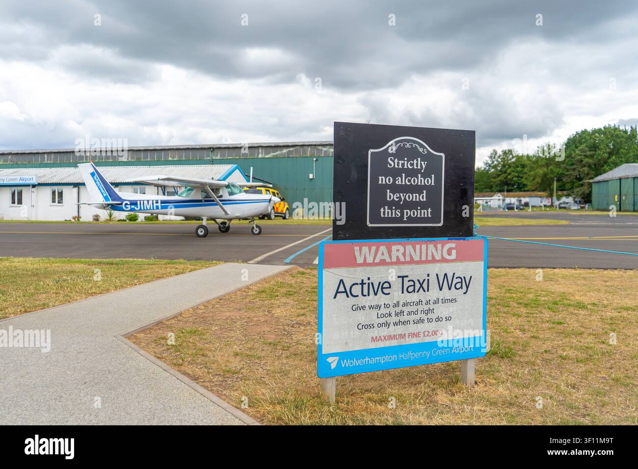 Vue rapprochée d'un panneau indiquant une voie de taxi active à l'aéroport de Wolverhampton Halfpenny Green alors qu'un avion passe en arrière-plan. Banque D'Images