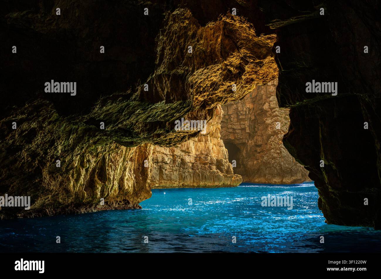 Grotte marine baignée de soleil avec eau turquoise et cavité côtière rocheuse encadrée par les ombres sombres des falaises Banque D'Images