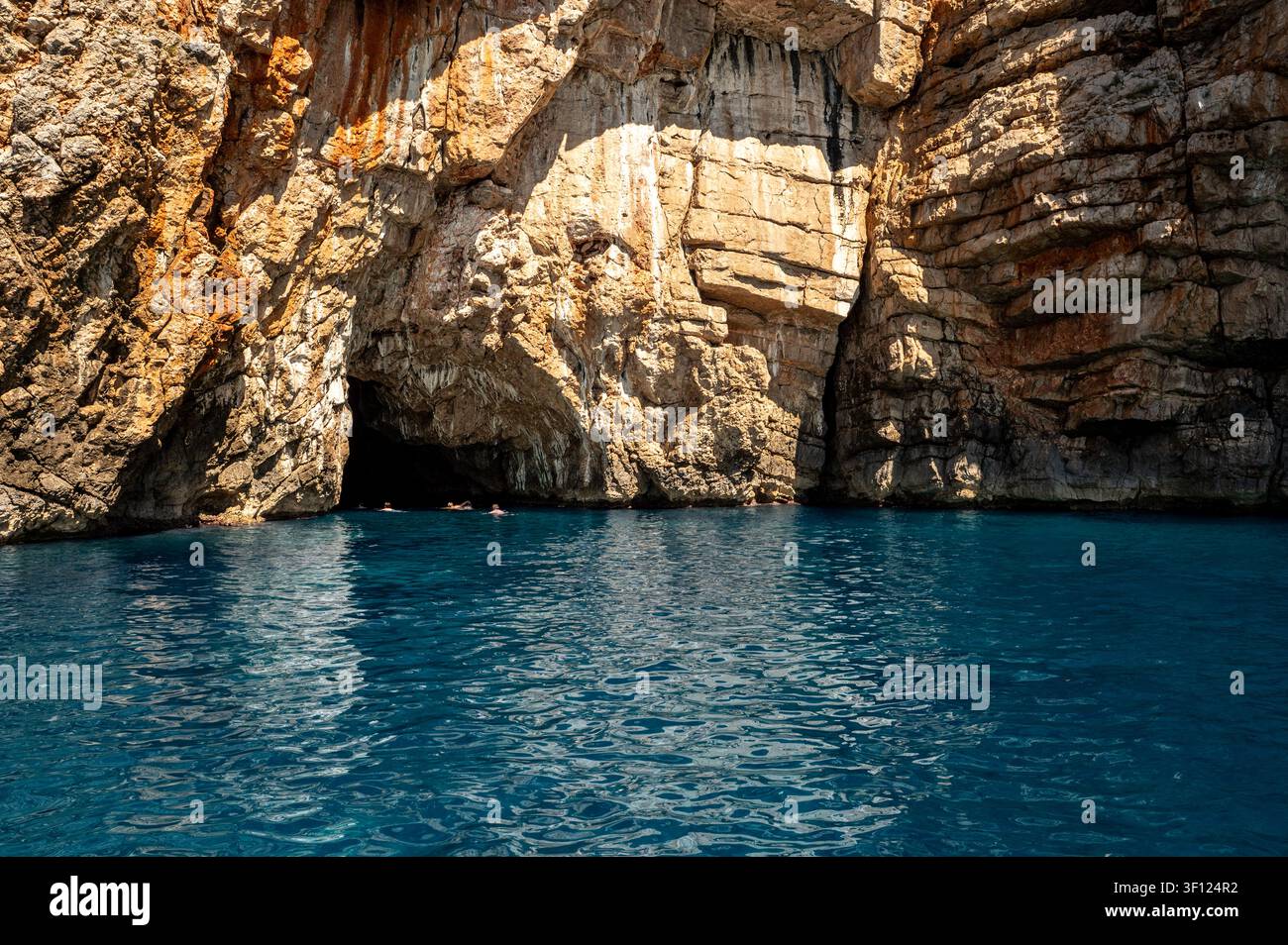 Entrée d'une grotte marine baignée de soleil avec eau turquoise et falaises calcaires abruptes ainsi que des nageurs Banque D'Images