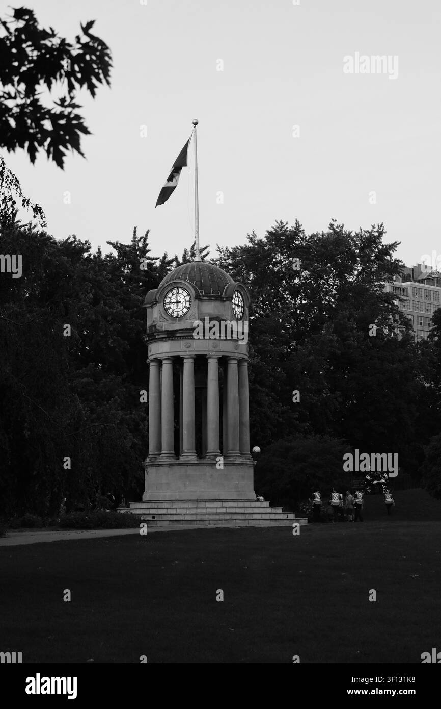 Monument d'horloge avec drapeau canadien à Victoria Park, entouré d'arbres, Kitchener, Ontario, Canada. Banque D'Images