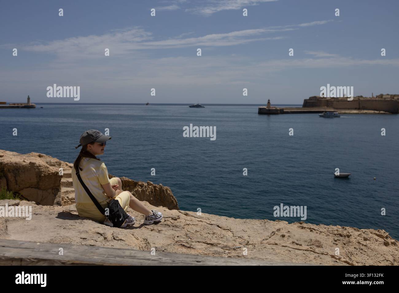 Femme assise sur une falaise rocheuse et regardant la baie du Grand Harbour à La Valette, Malte, le 19 juin 2026 Banque D'Images