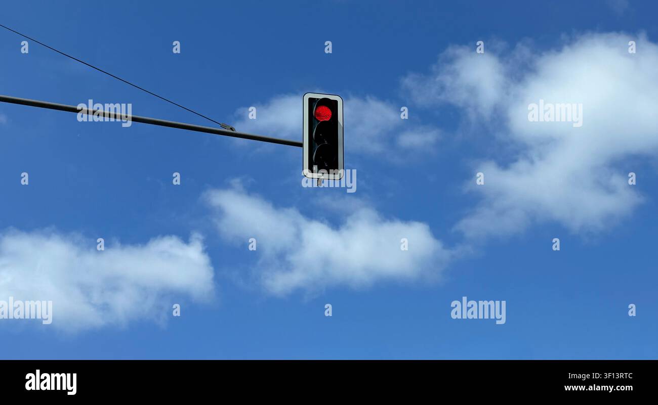 Feu rouge suspendu à un poteau devant un ciel bleu parsemé de nuages Banque D'Images