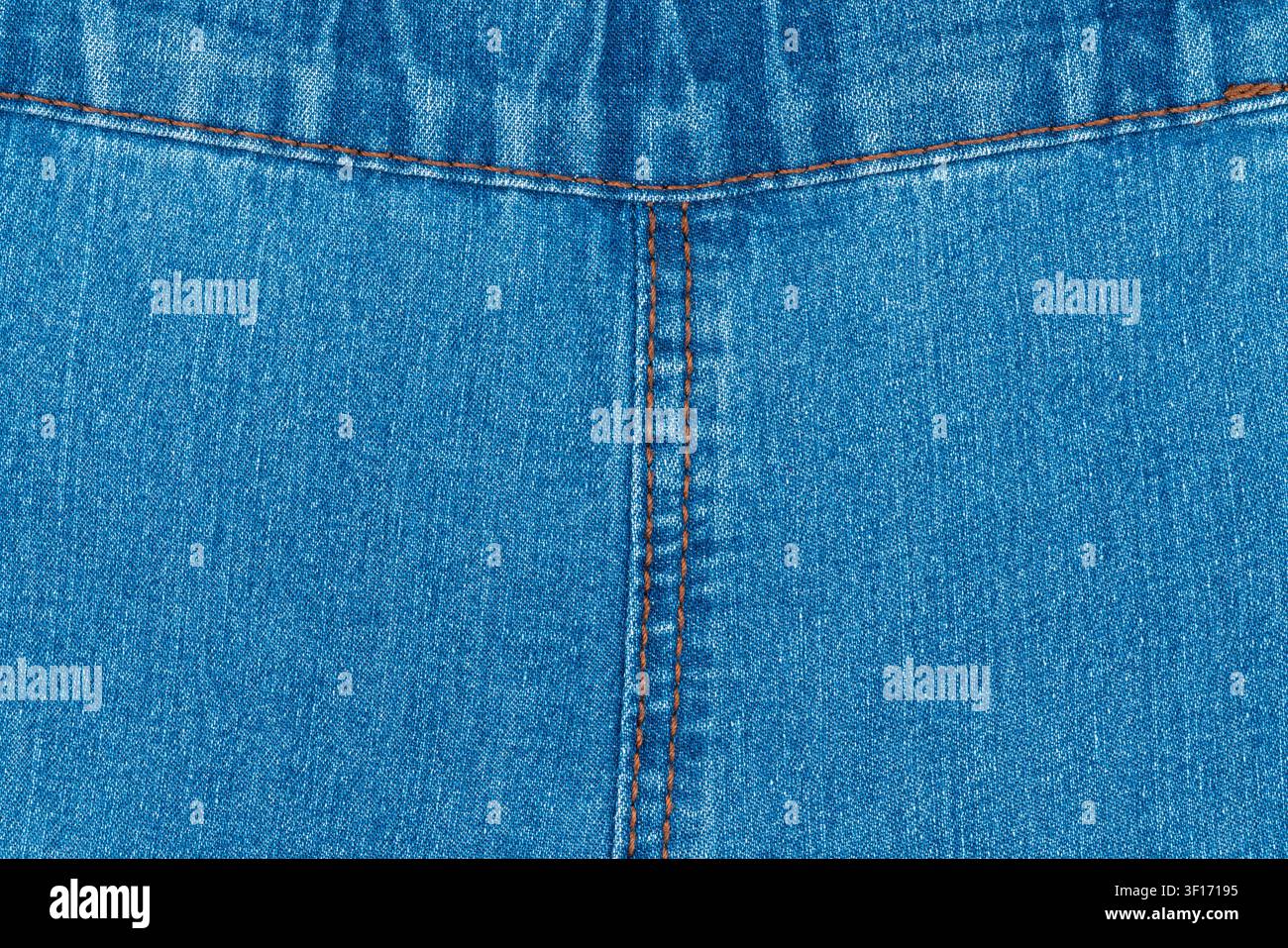 Tissu de jean bleu classique. Composition symétrique montrant la couture centrale et les points orange. Le matériau denim texturé constitue un fond parfait pour la mode Banque D'Images