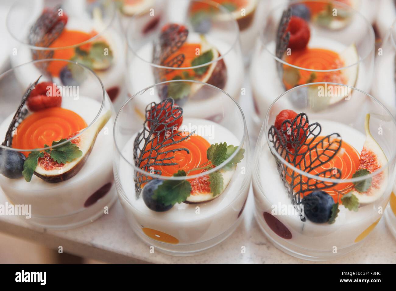 Des desserts délicats dans des verres transparents aux couleurs vives. Les oranges, les baies et les garnitures au chocolat ajoutent de l'élégance. Parfait pour les événements haut de gamme ou le luxe Banque D'Images