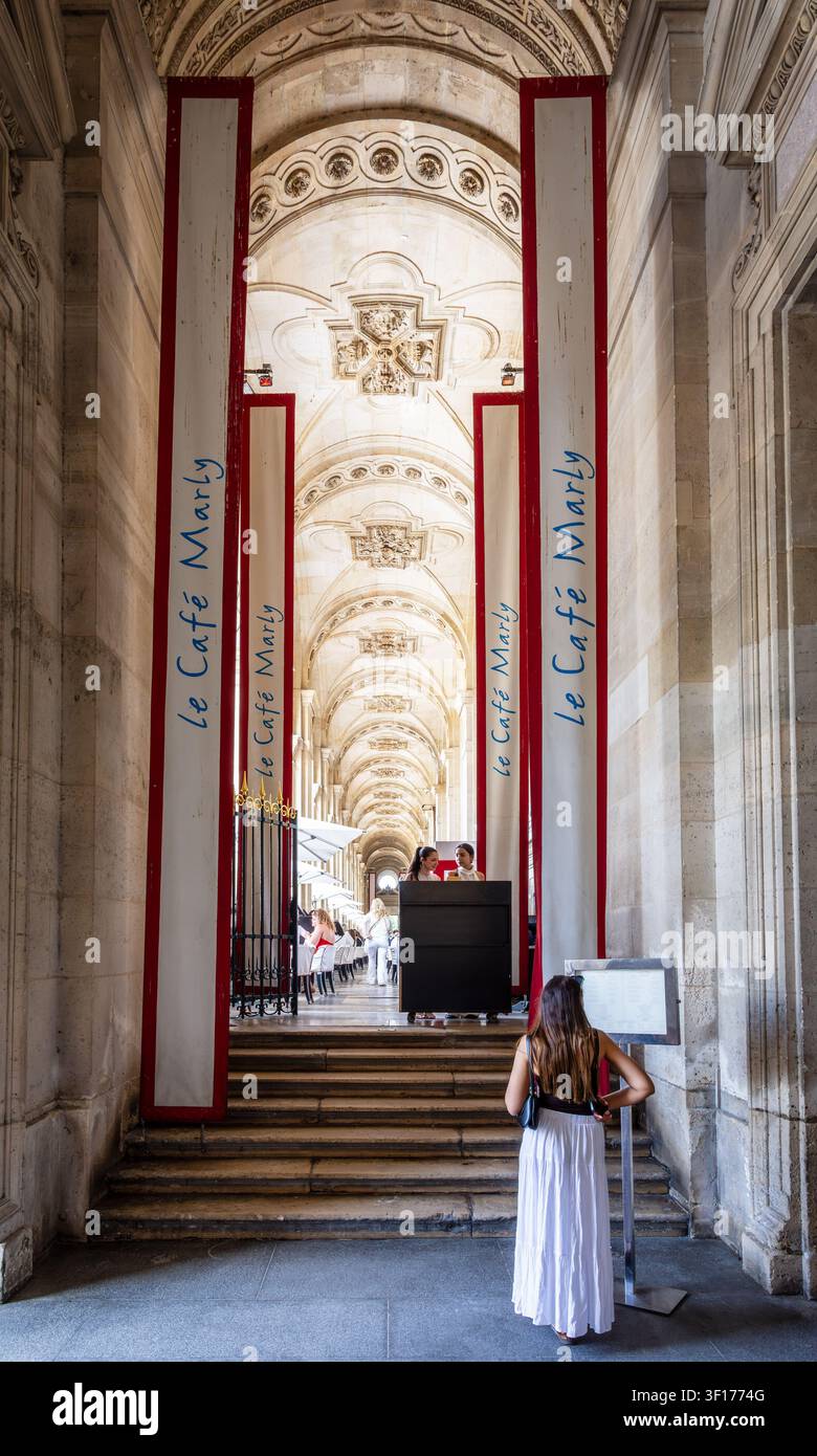 Une femme en robe d'été jette un coup d'œil au menu à l'entrée du Café Marly à Paris, en France, un restaurant célèbre situé dans le palais du Louvre. Banque D'Images