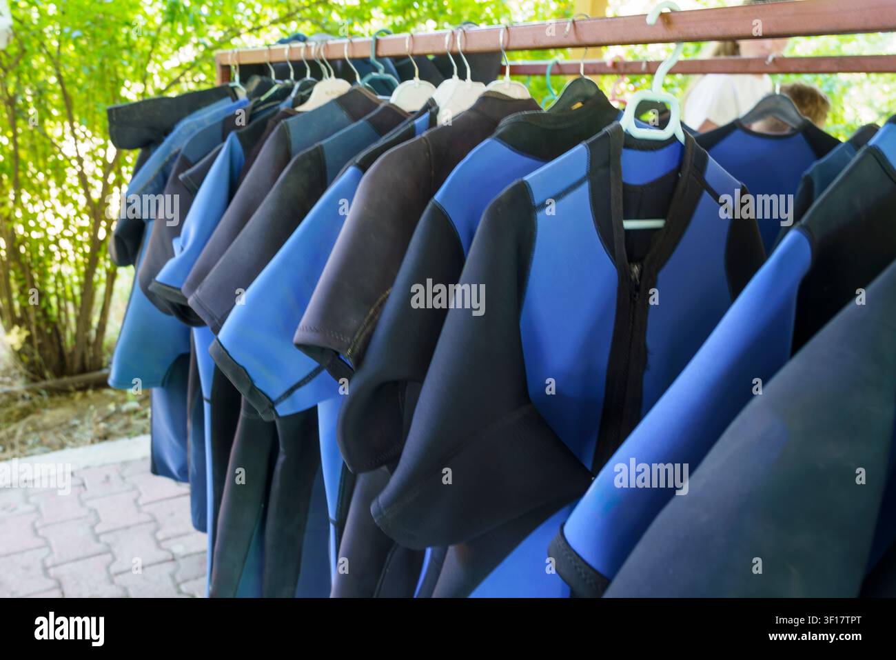 Combinaisons de plongée exposées sur un rack dans un cadre extérieur ombragé, proposant une variété de tailles et de couleurs pour le surf et les activités nautiques Banque D'Images