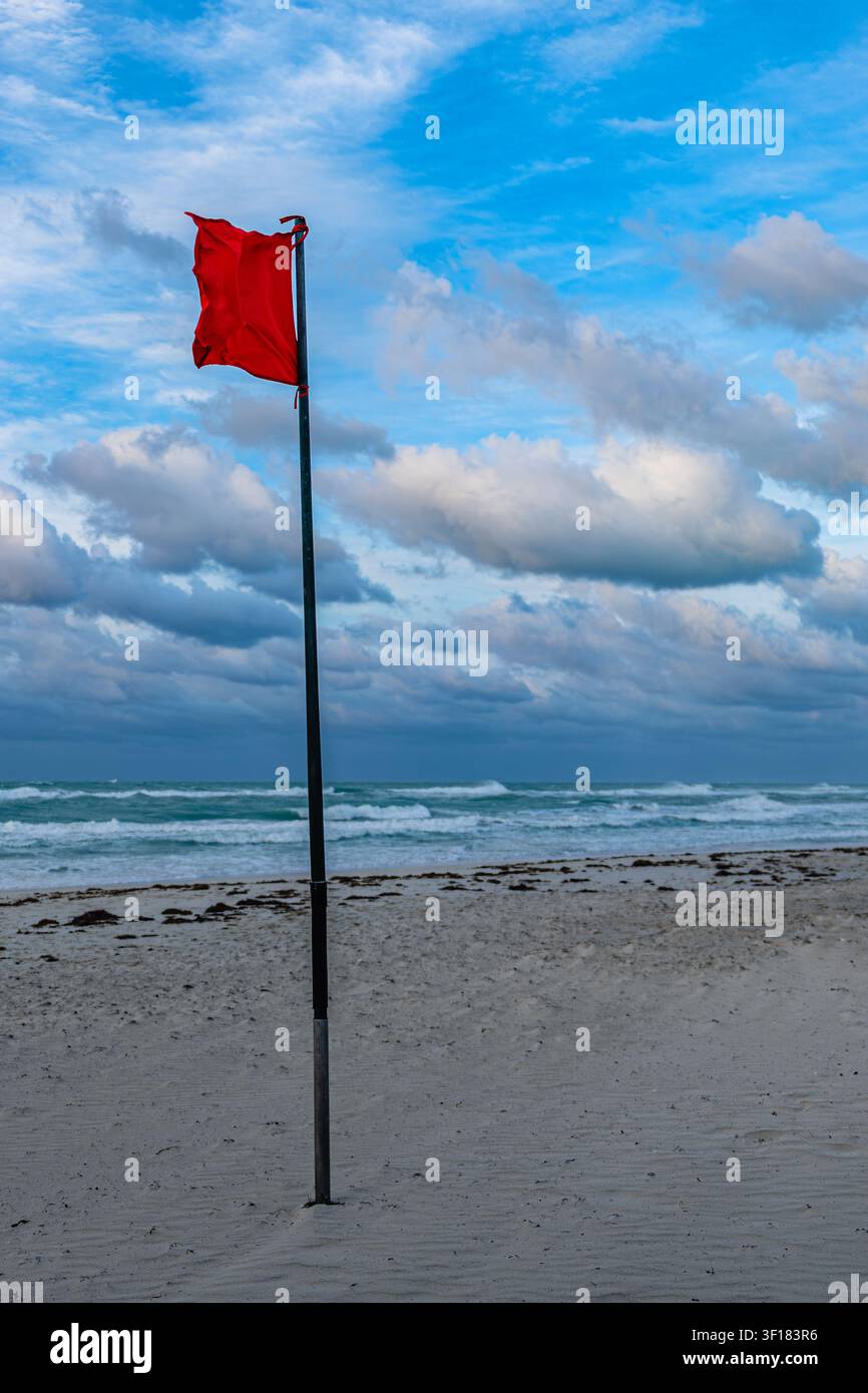 Drapeau d'avertissement rouge debout sur une plage avec ciel nuageux et vagues. Banque D'Images