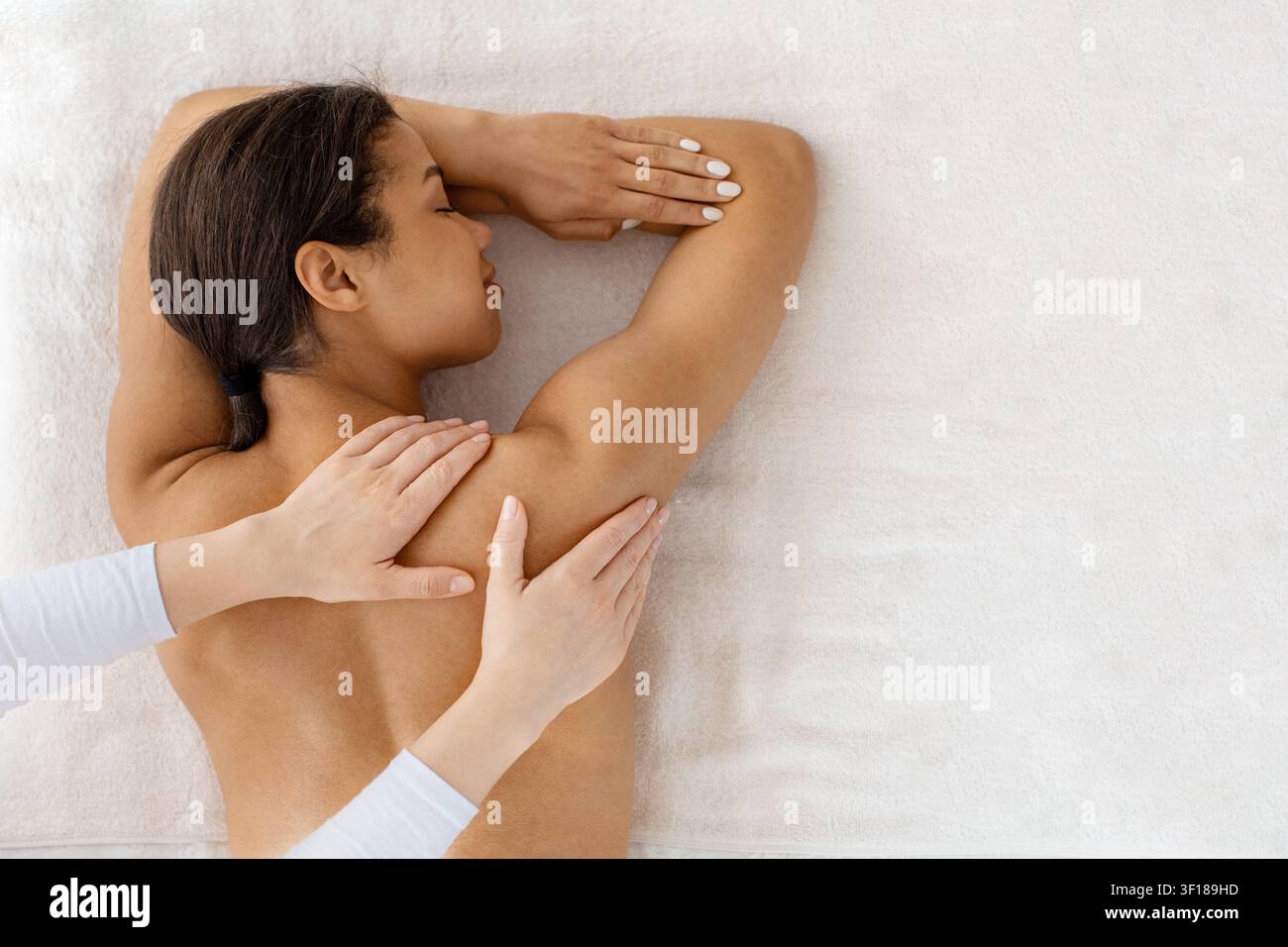 Jeune femme noire recevant un massage doux des épaules et du dos sur un lit de spa Banque D'Images