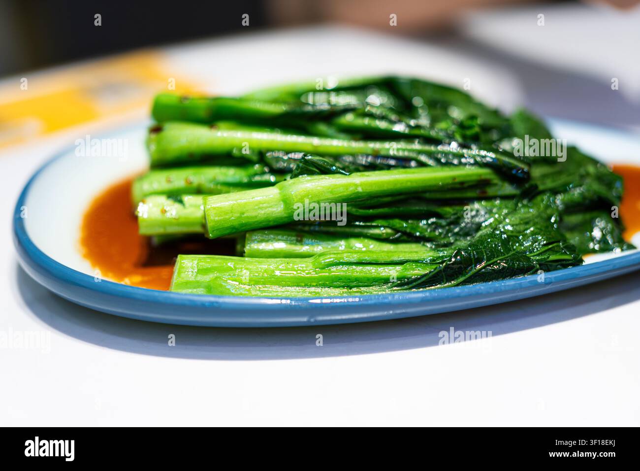 Brocoli chinois cuit à la vapeur avec sauce aux huîtres dans une assiette à bordure bleue, plat dim sum cantonnais typique Banque D'Images