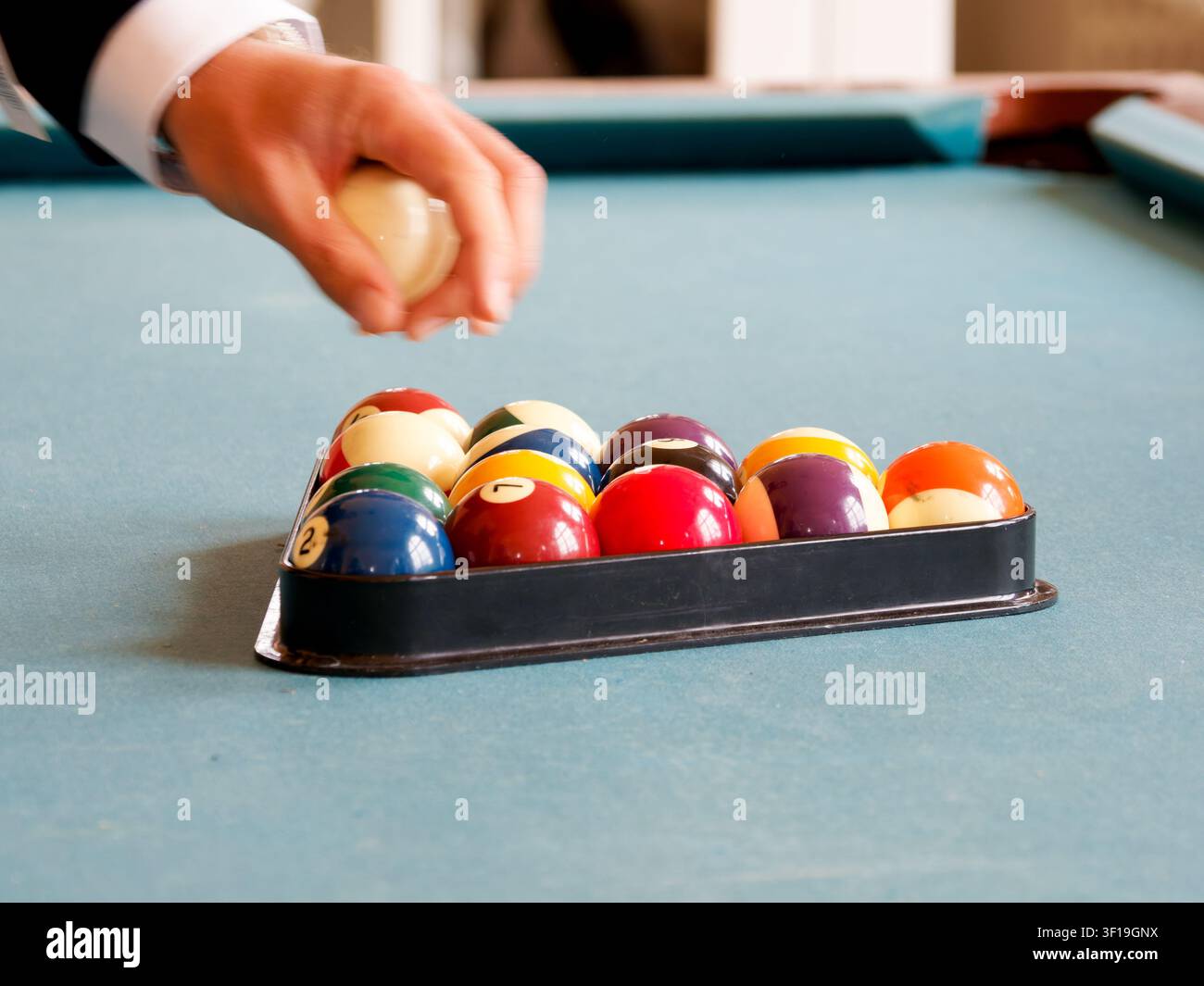 Billes de billard disposées en triangle sur une table de billard, avec un joueur tenant la boule de jeu Banque D'Images