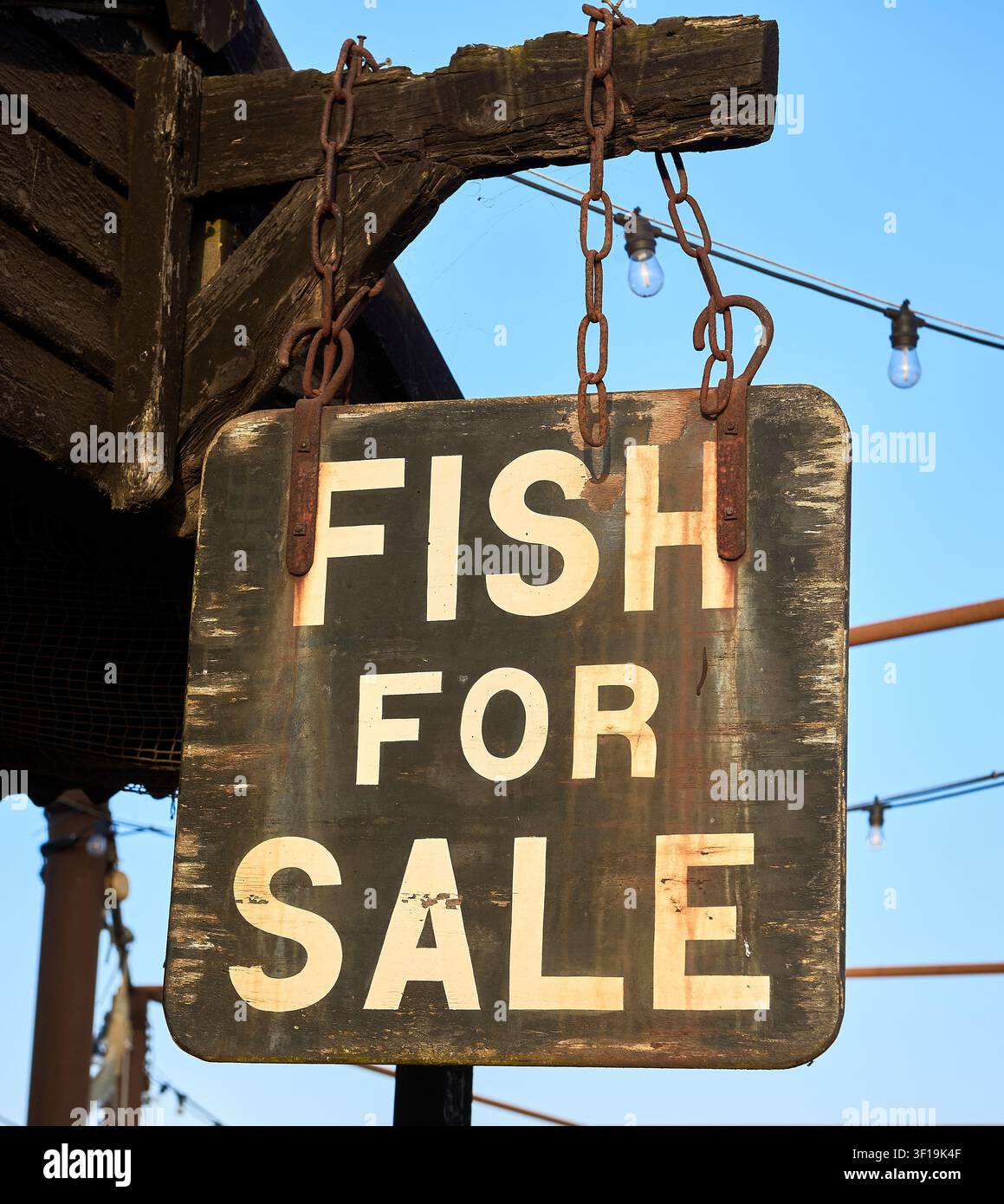Un panneau en bois rustique usé portant l'inscription "Fish For Sale" suspendu à des chaînes rouillées au port de Southwold, Suffolk, Angleterre. Banque D'Images
