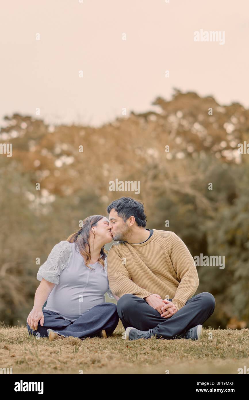 Moment de maternité automnal rempli d’amour alors qu’un couple enceinte partage un tendre baiser en plein air, mettant en valeur l’affection, l’attente et les chaudes couleurs saisonnières Banque D'Images