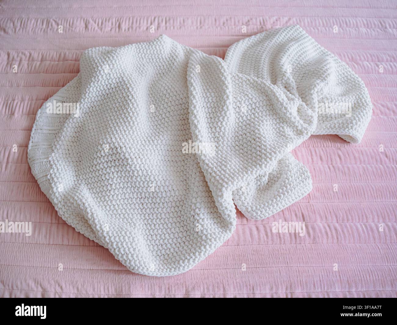 La couverture en laine tricotée lourde avec le motif de points texturés gît froissée sur la couverture en tissu matelassée sur le lit dans l'intérieur de la pièce. Banque D'Images