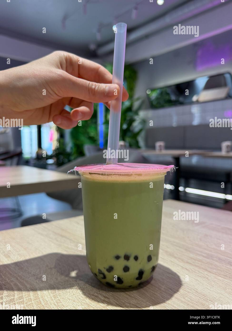 Thé à bulles au matcha avec perles de tapioca sur la table du café tandis qu'une main place une paille large dans la boisson. Culture café, tendance alimentaire, style de vie, rafraîchissement Banque D'Images