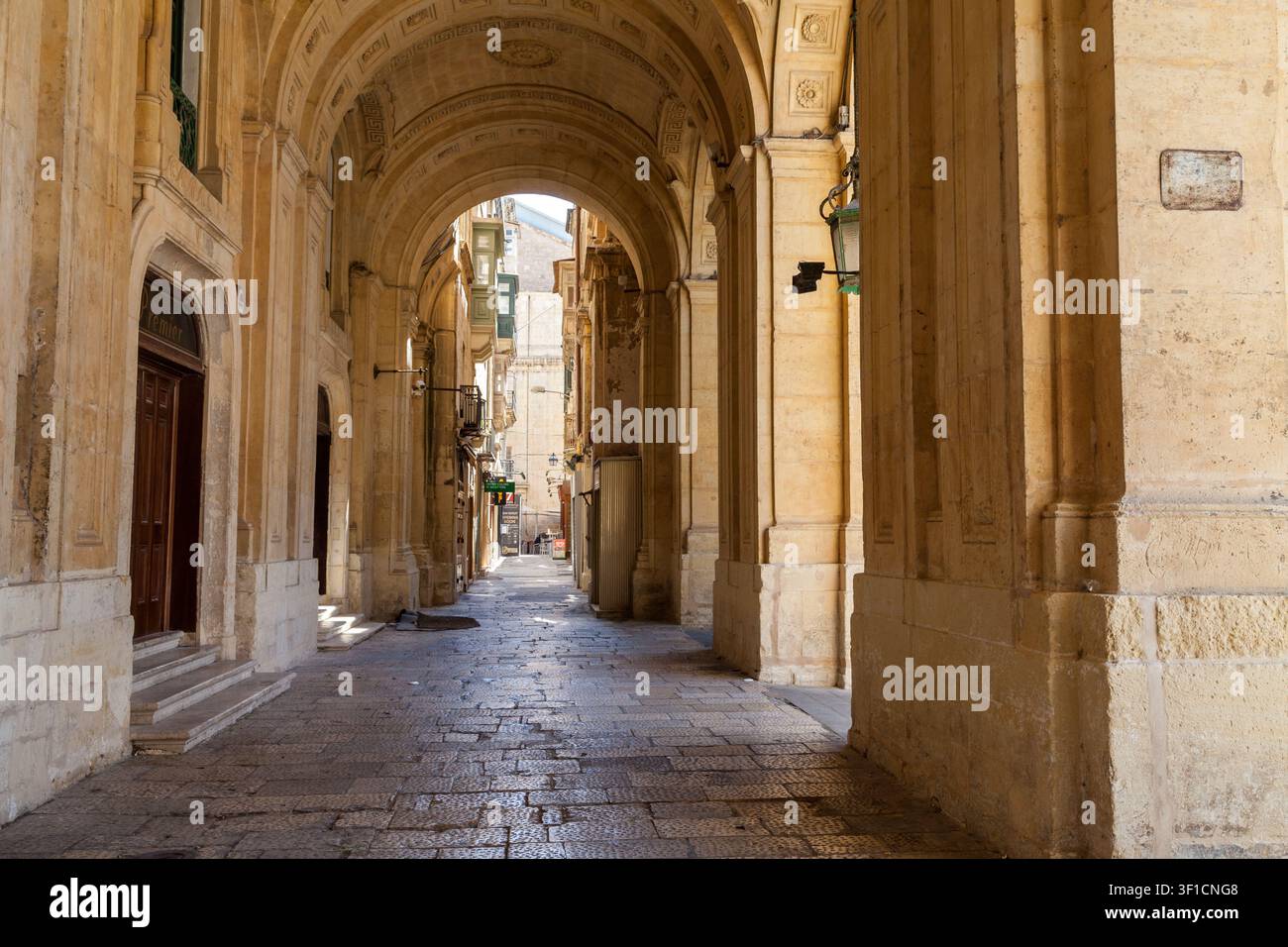 Une arche de pierre ombragée mène à travers un passage pavé bordé d'architecture en calcaire ornée près de la Bibliothèque nationale, Valletta, Malte Banque D'Images