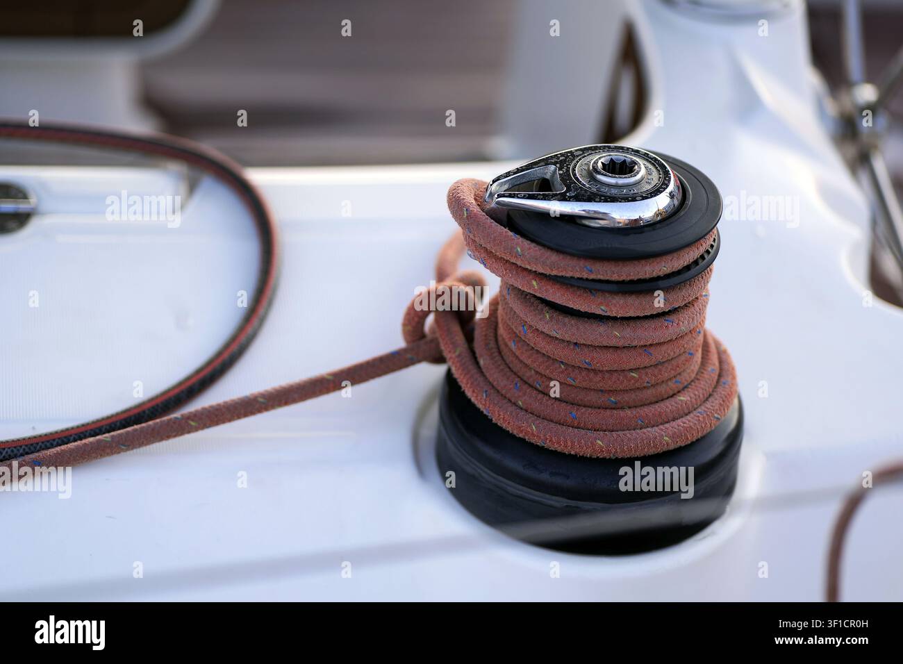 Winch de bateau à voile avec une corde orange soigneusement enroulée sur son tambour, prête à gérer le gréement du bateau, mettant en valeur l'équipement marin de près sur le pont d'un yacht Banque D'Images