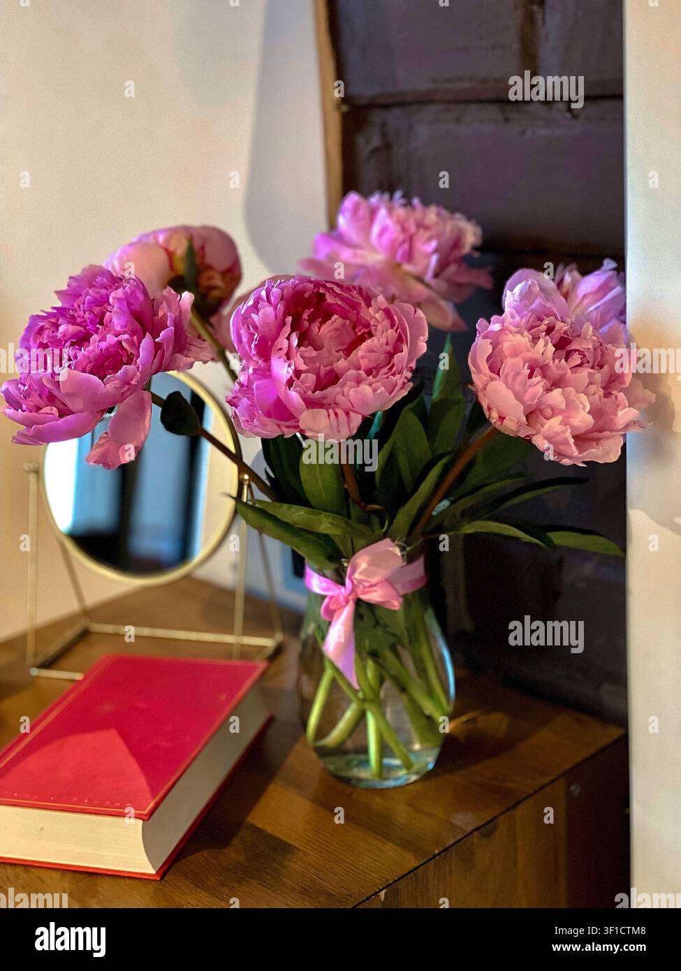 Pivoines roses fraîches dans un vase en verre sur une table en bois avec un intérieur chaleureux. - Image de stock capturée avec un smartphone