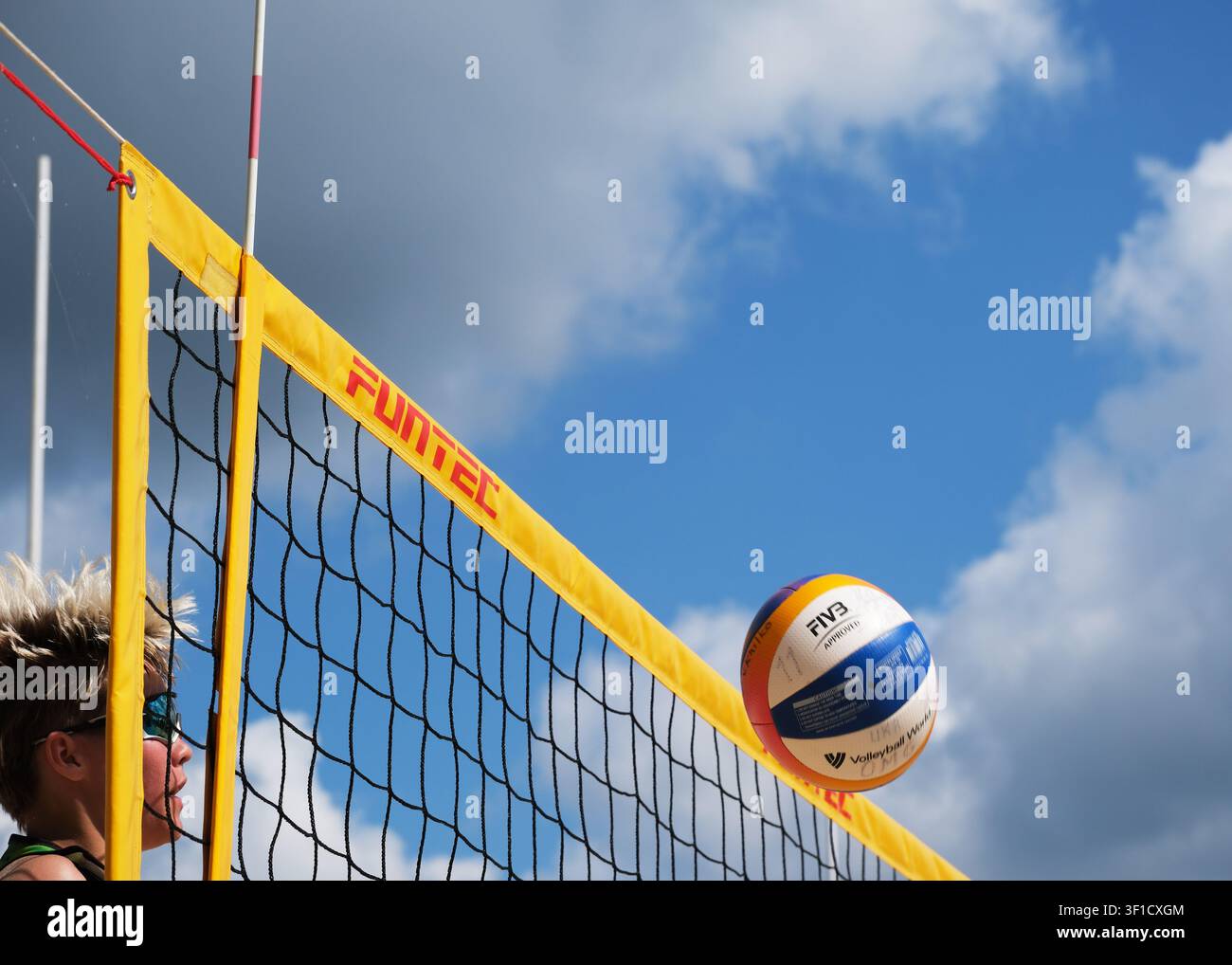 KIEV, UKRAINE, 12 juillet 2026. Le beach-volley vole au-dessus du filet lors d’un tournoi en extérieur 2 contre 2 sur un terrain de sable sous un ciel d’été dramatique. Banque D'Images