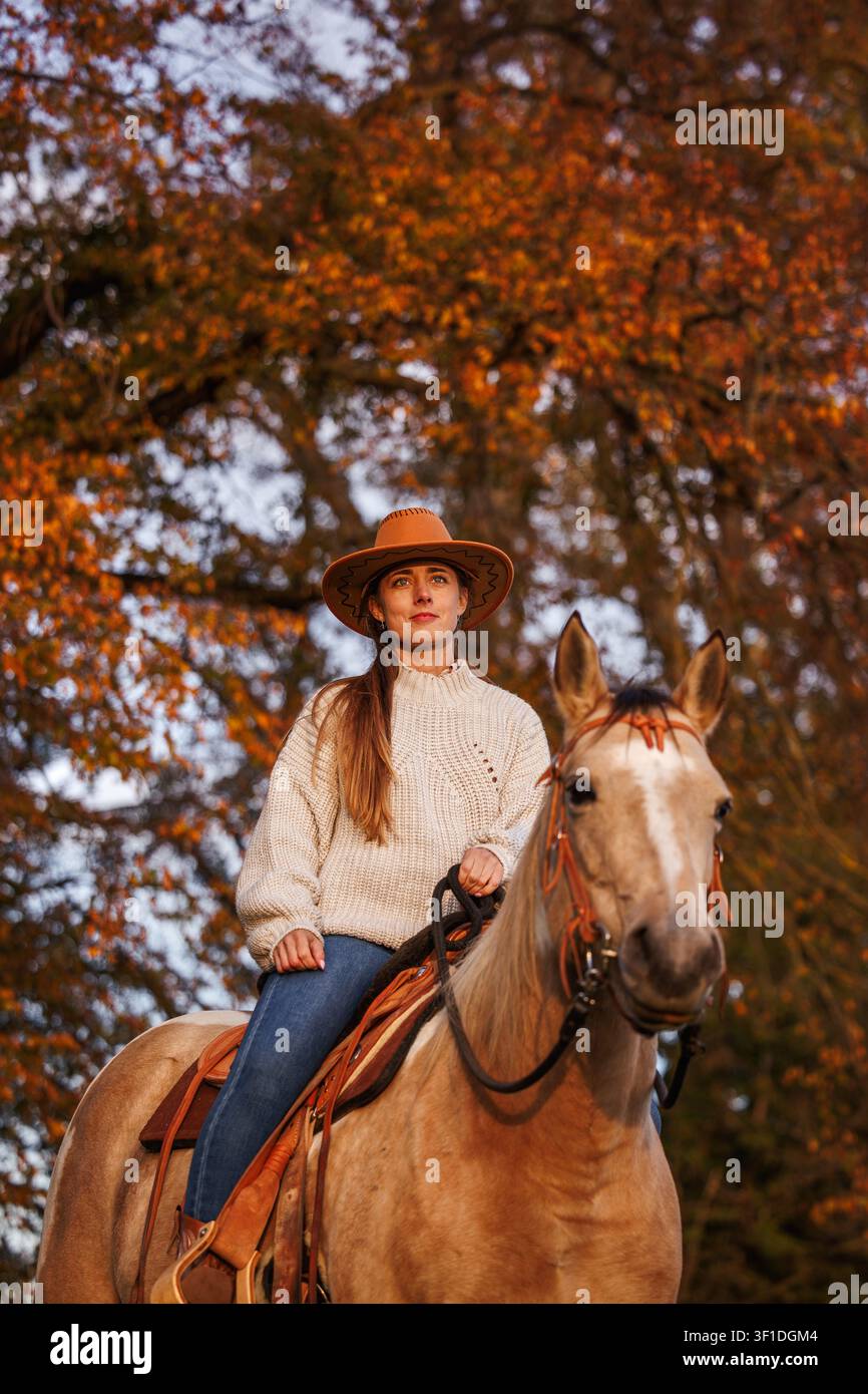 Cow-girl montant à cheval dans la nature automnale au coucher du soleil. Femme en chapeau de cowboy assise sur un cheval profitant du style de vie western Banque D'Images