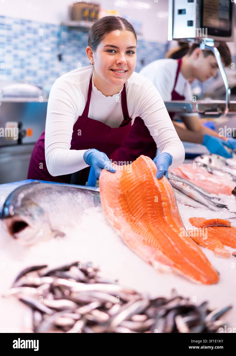 Une vendeuse réactive qui fait la démonstration d'un morceau de saumon dans un magasin de poisson Banque D'Images