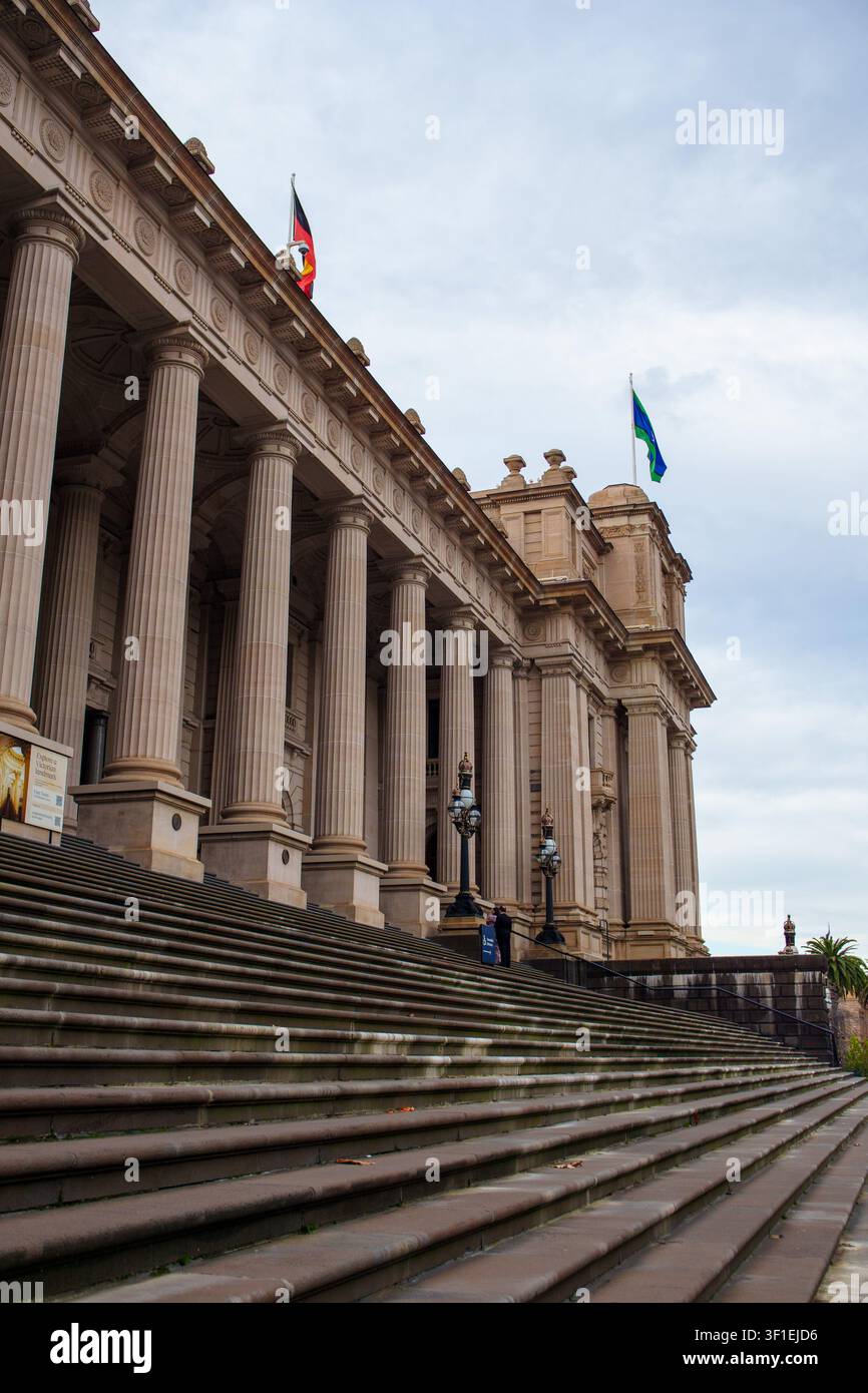 Une vue en contre-plongée d'un bâtiment néoclassique monumental présentant des colonnes imposantes, des escaliers en pierre et un éclairage orné sous un ciel sombre et couvert. Banque D'Images