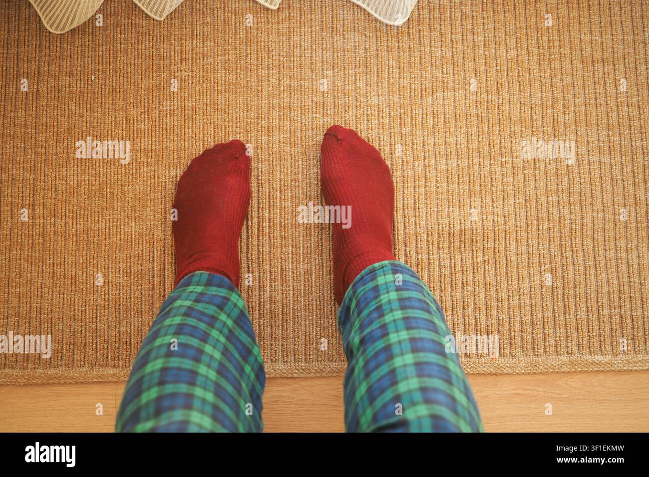 Pieds chaussés de chaussettes rouges sur un tapis tissé avec un pantalon à carreaux Banque D'Images