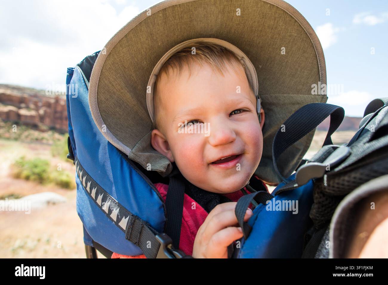 Un tout-petit heureux sourit depuis un porte-bébé à dos Banque D'Images