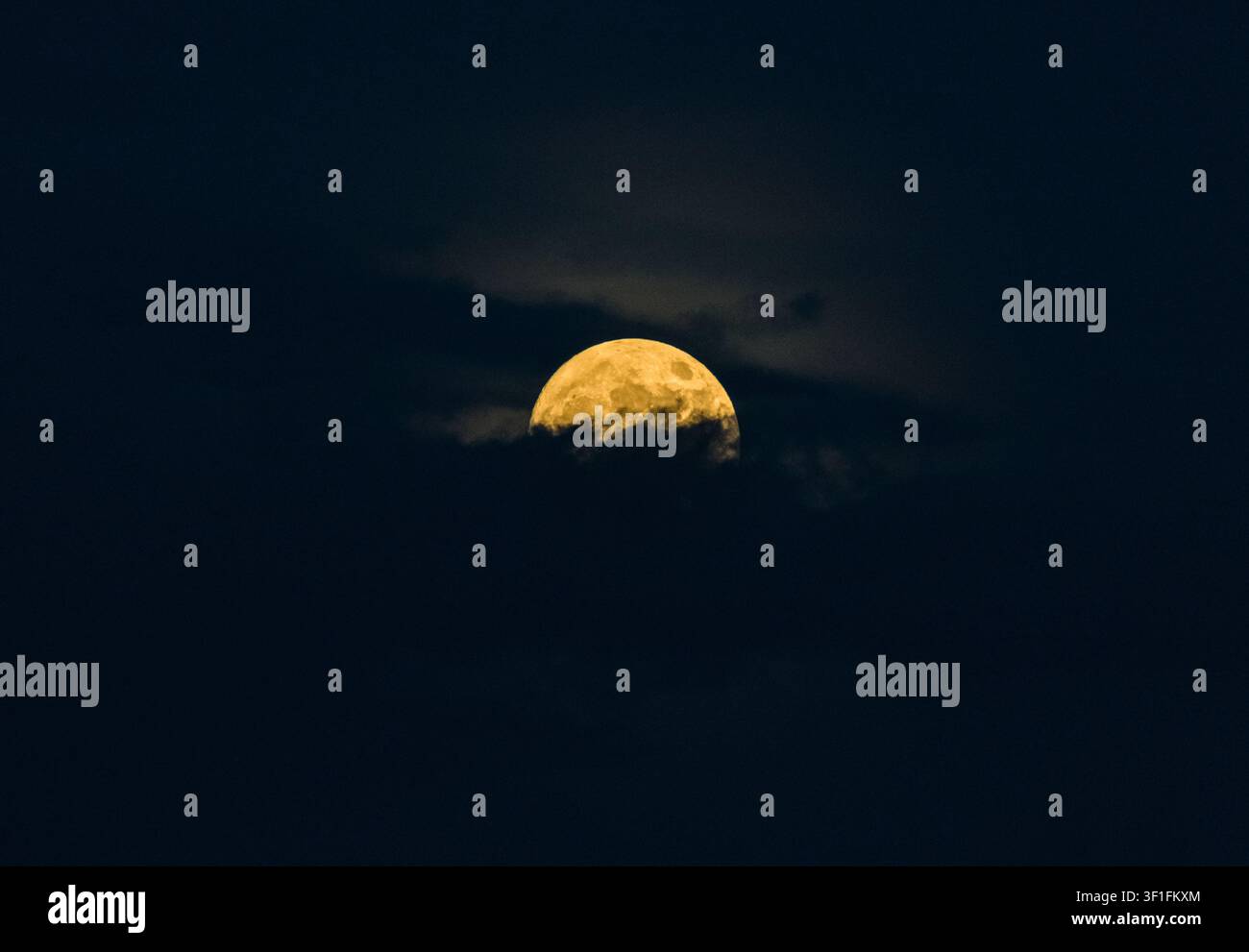 Lune pleine jaune brillante qui brille à travers les nuages du ciel nocturne Banque D'Images