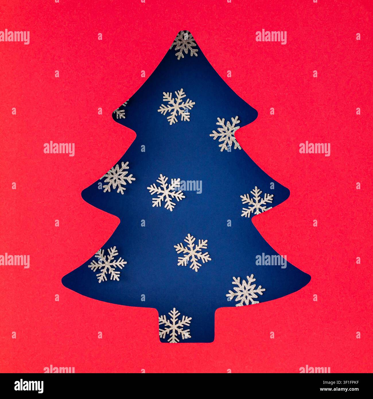 Composition hivernale créative avec une découpe d'arbre de Noël décorée de flocons de neige blancs sur fond bleu. Disposition festive avec espace libre. Banque D'Images