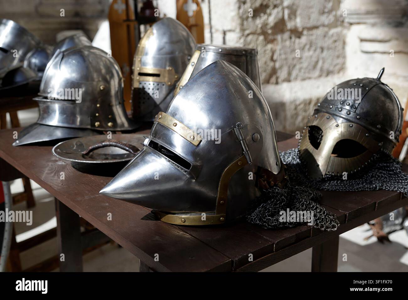 Collection de casques en métal médiévaux exposés sur une table en bois dans un cadre historique. Banque D'Images