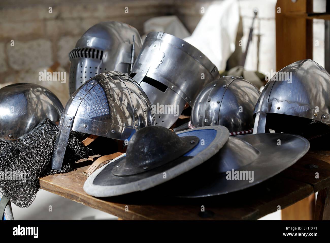 Collection de casques en métal médiévaux exposés sur une table en bois dans un cadre historique. Banque D'Images