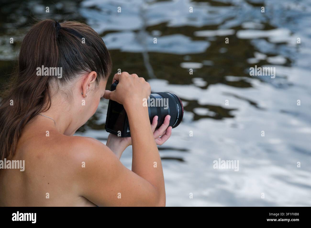 KIEV, UKRAINE, 12 juillet 2026, Une photographe examine les images capturées sur un appareil photo numérique tout en se tenant près de l'eau lors d'un photographe en plein air Banque D'Images