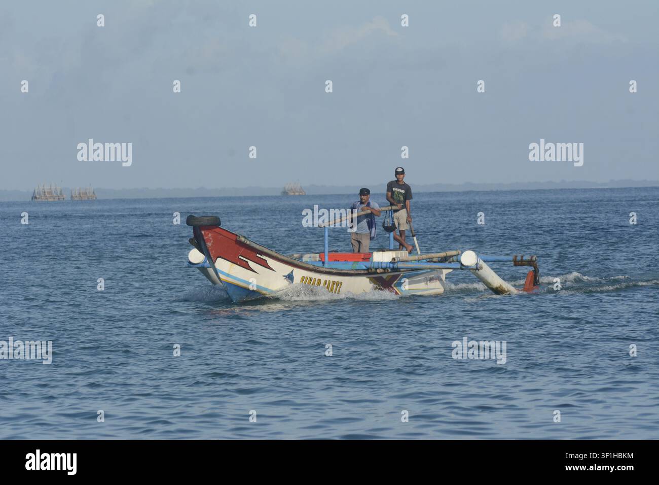 Pêcheurs traditionnels indonésiens manœuvrant un petit bateau de pêche en bois à moteur à balancier étiqueté Sinar Sakti sur les eaux bleues de l'océan à Ujung Kulon Banque D'Images
