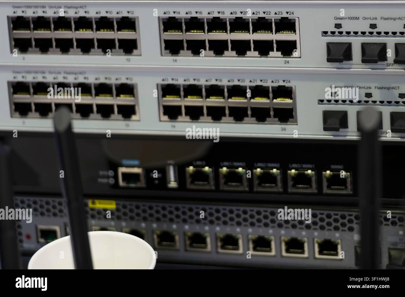 Vue avant d commutateurs réseau empilés avec des rangées de ports Ethernet et des appareils équipés d'antennes au premier plan. Banque D'Images