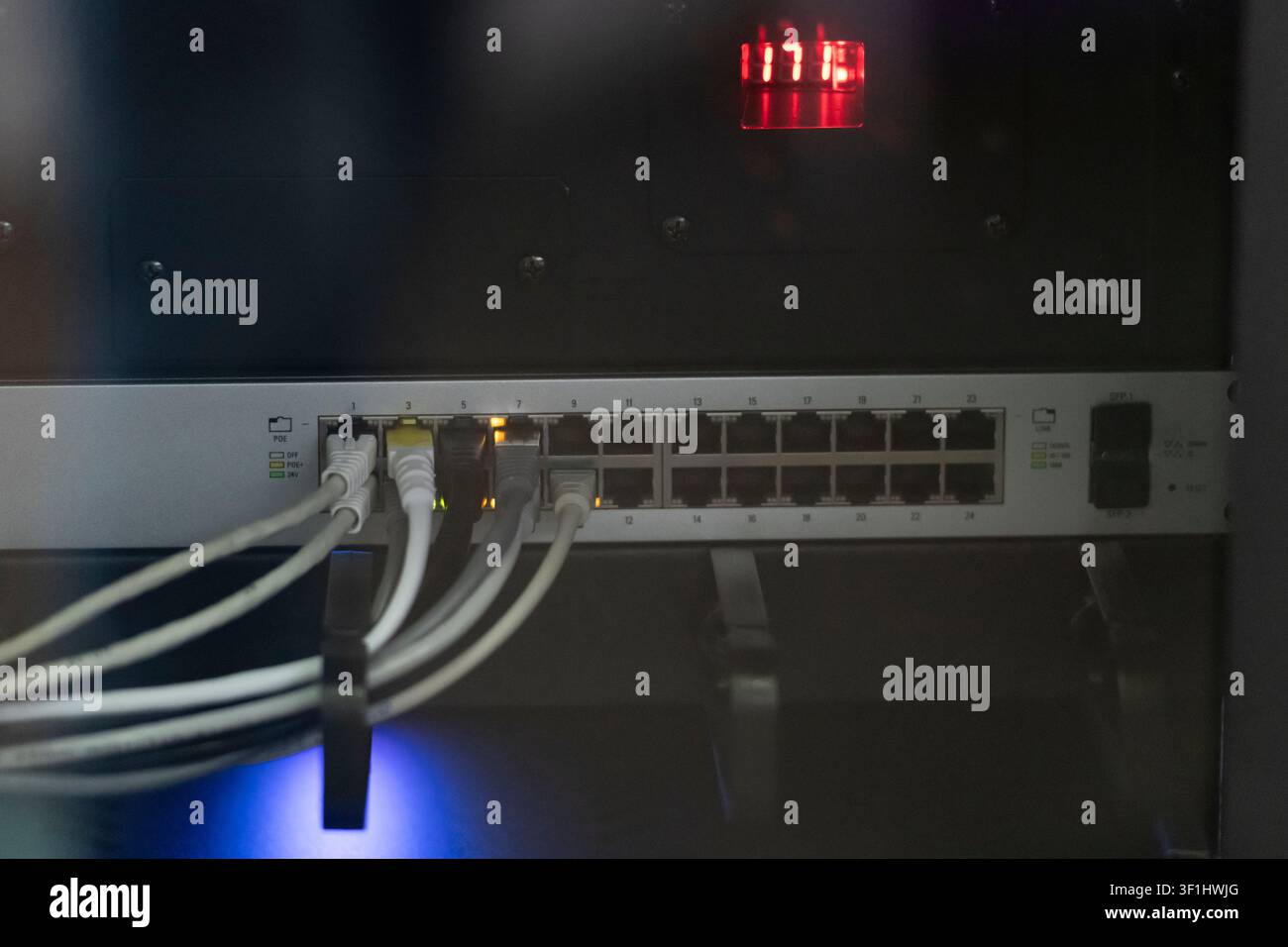 Commutateur réseau avec câbles Ethernet blancs connectés à l'intérieur d'un rack d'équipement sombre, avec voyants d'état illuminés. Banque D'Images