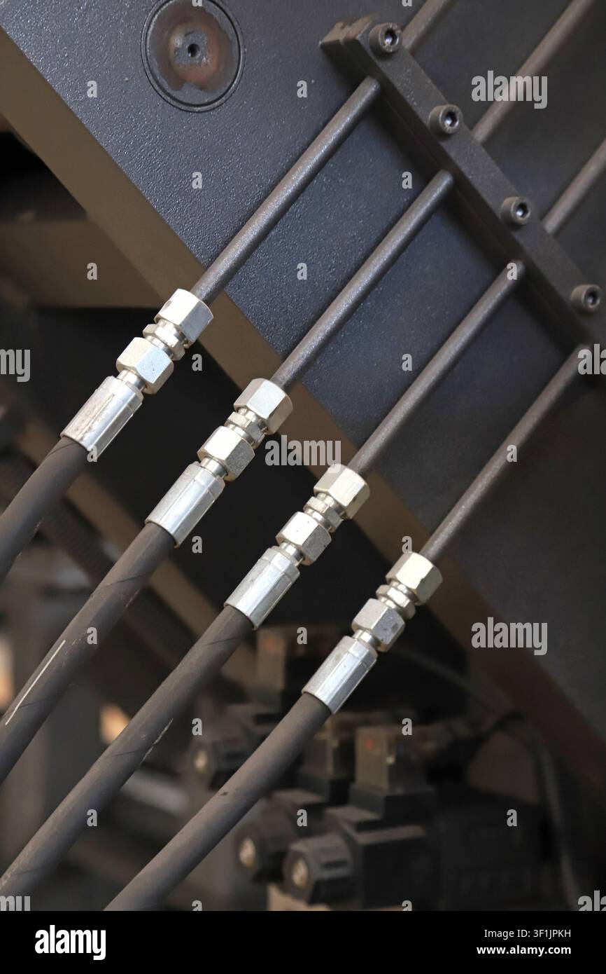 L'image montre des tuyaux hydrauliques soigneusement disposés sur un équipement industriel. Des raccords en métal argenté, des tuyaux noirs et des supports métalliques forment une mécanique précise Banque D'Images