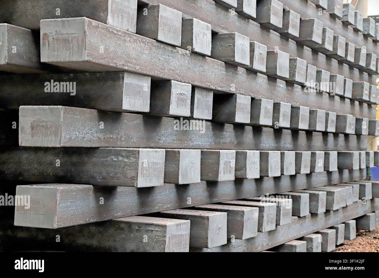 Cette photographie haute résolution capture les piles lourdes et texturées de billettes d'acier rectangulaires dans un entrepôt d'aciérie. L'image met en valeur le ra Banque D'Images