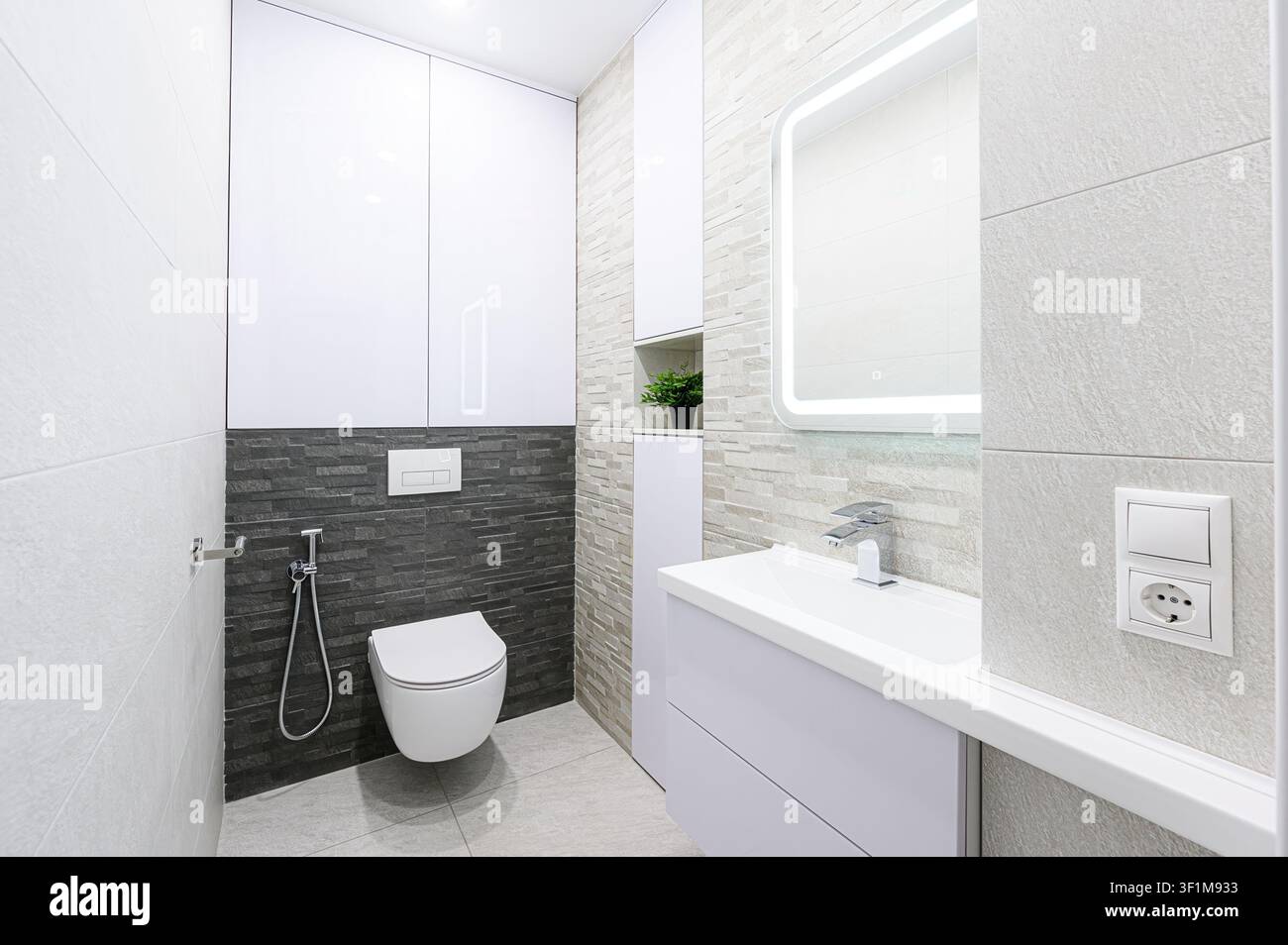 salle de bain moderne et minimaliste aux tons gris et blanc, dotée d'une toilette flottante, d'un évier épuré et d'un miroir LED Banque D'Images