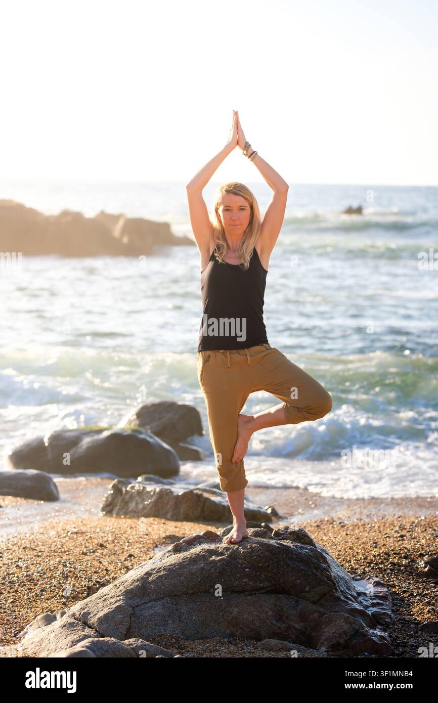 Femme en équilibre dans la pose de l'arbre du yoga, trouvant bien-être et pleine conscience sur une plage Banque D'Images