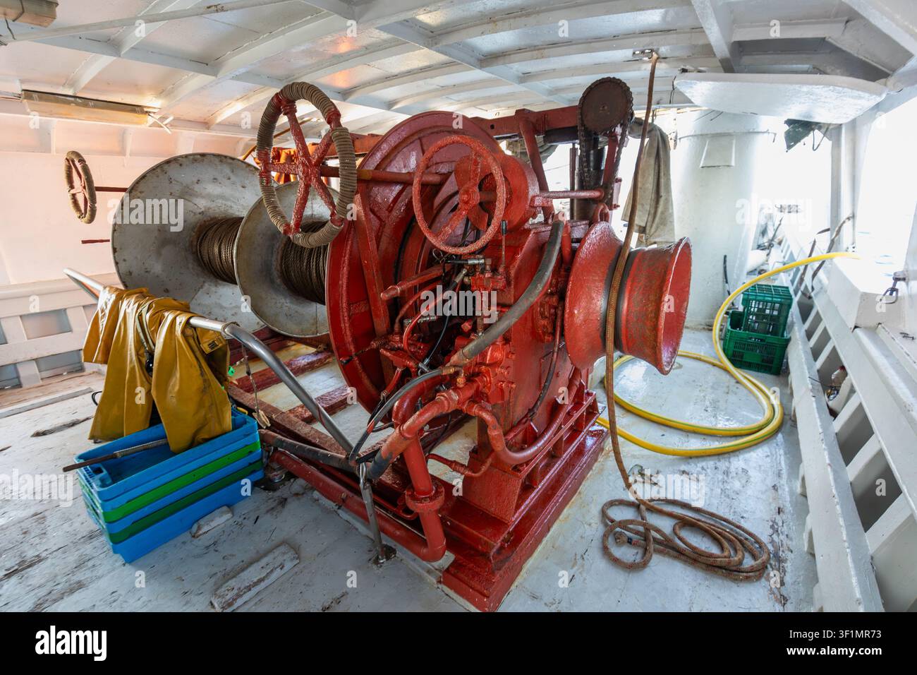 Grossissement d'une winch industrielle rouge avec câble en acier et tuyaux hydrauliques à l'intérieur d'une zone de travail sur le pont d'un navire, montrant un équipement maritime robuste utilisé pour à Banque D'Images