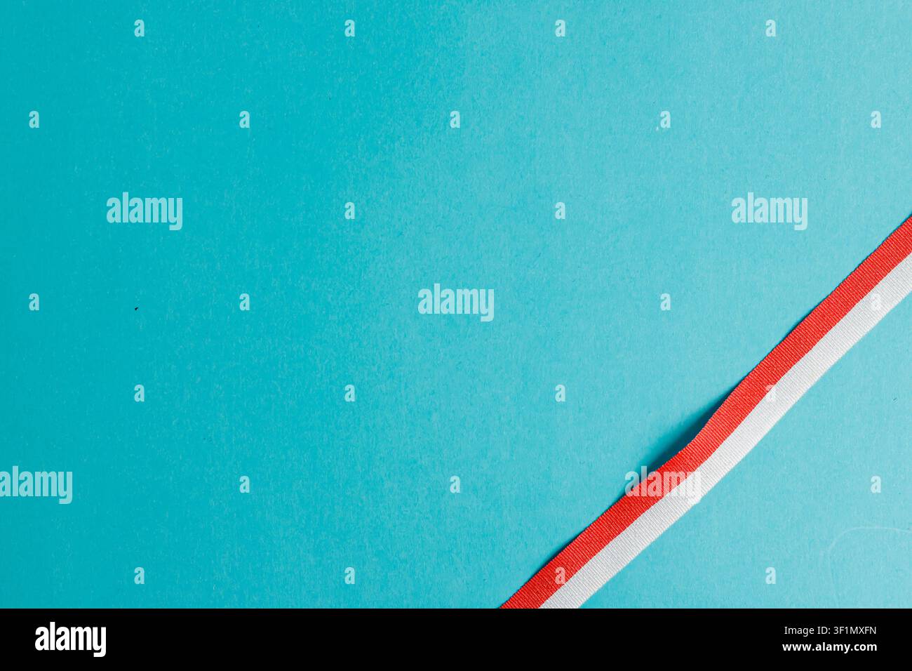 Un ruban rayé rouge et blanc en diagonale positionné sur un fond bleu cyan vif. Élément de conception minimaliste idéal pour les cartes du jour de l'indépendance indonésienne, les célébrations nationales et les bannières avec espace de copie. Photo de haute qualité Banque D'Images