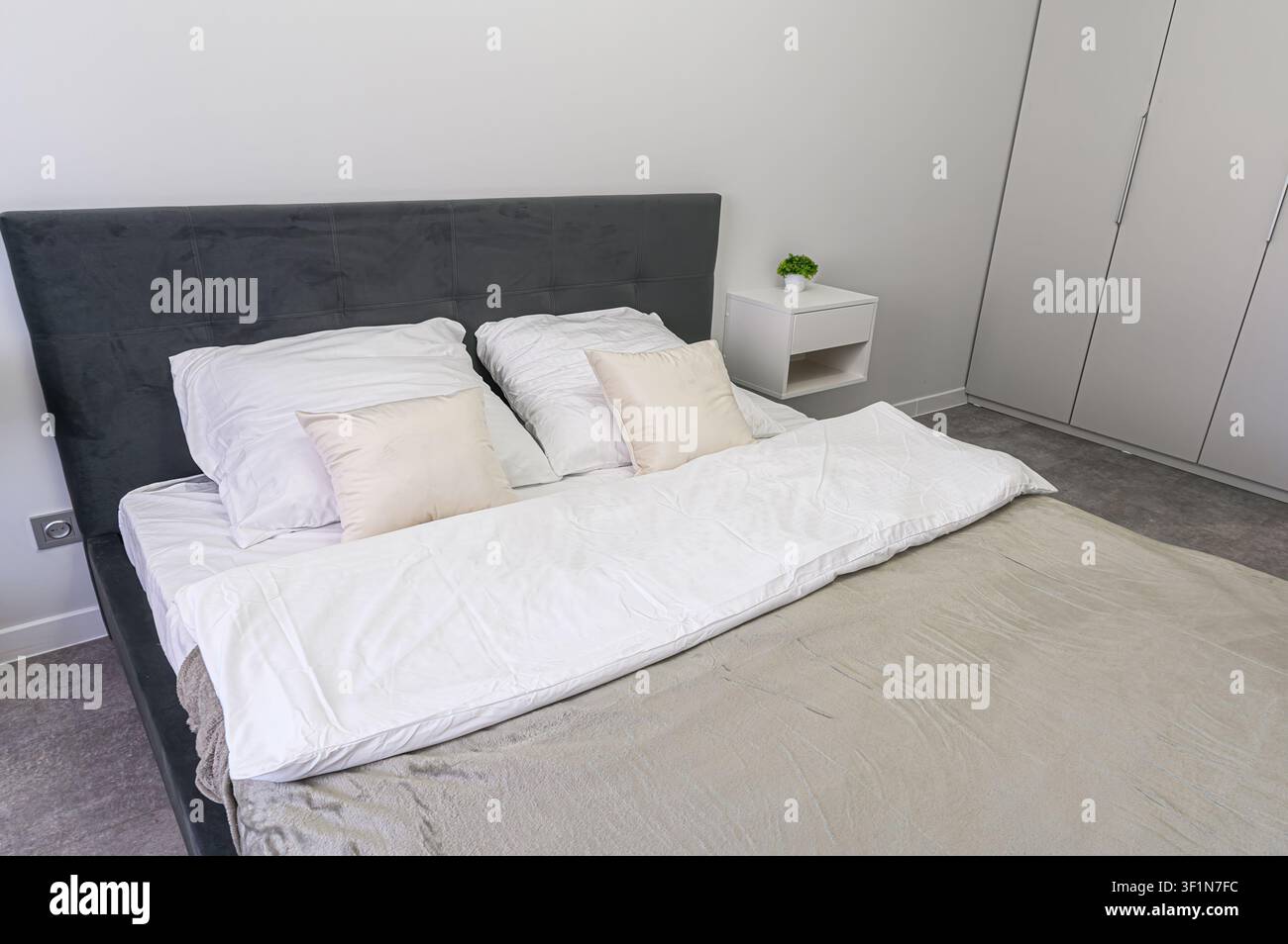 La chambre minimaliste présente un lit gris avec une literie blanche, complété par des oreillers blancs. Une table de chevet blanche avec une petite plante est posée à côté du lit. Gr Banque D'Images