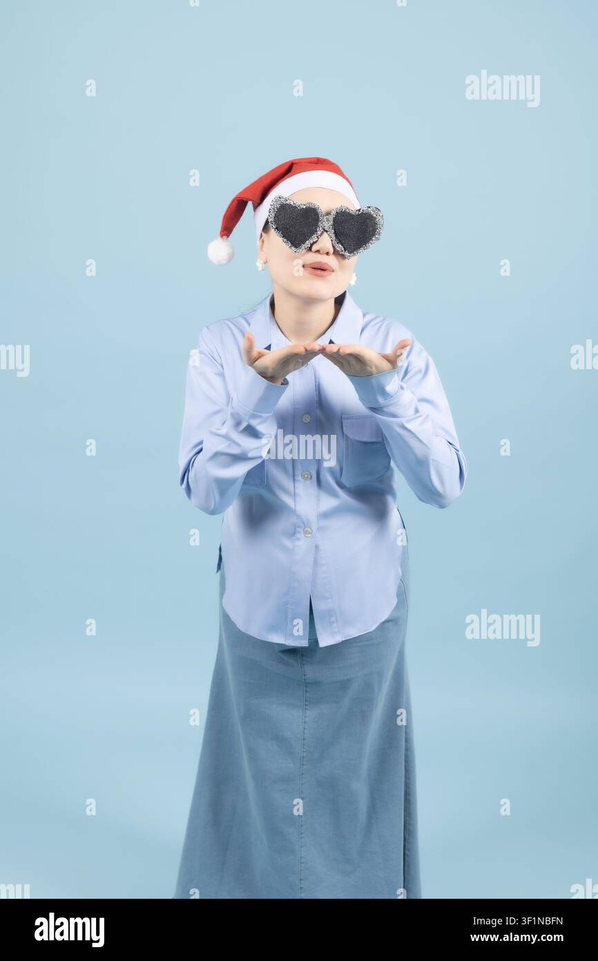 Jeune femme confuse portant un chapeau de Père Noël et des lunettes de soleil, regardant au loin dans le studio Banque D'Images