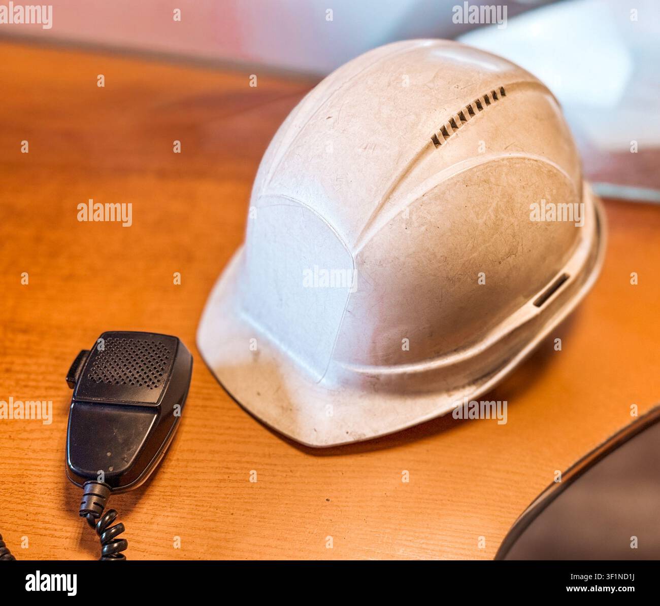 Casque de sécurité blanc industriel à côté d'un microphone de radio bidirectionnelle sur un bureau en bois. - Image de stock capturée avec un smartphone