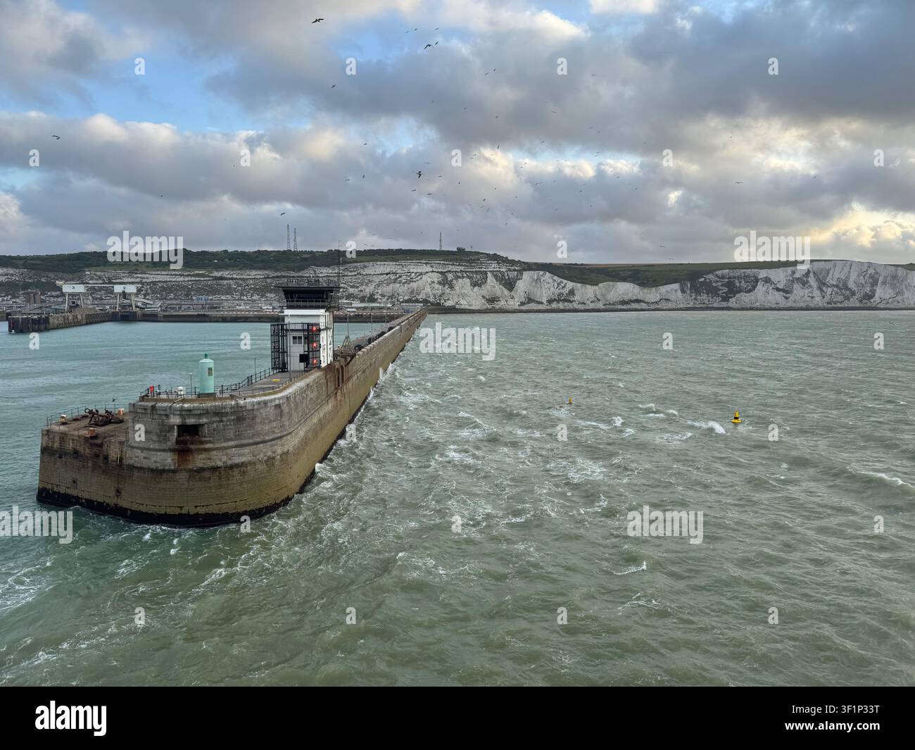 Un brise-lames s'étend dans la mer au port de Dover et les falaises blanches emblématiques en arrière-plan. Le ciel est sombre au petit matin - Image de stock capturée avec un smartphone